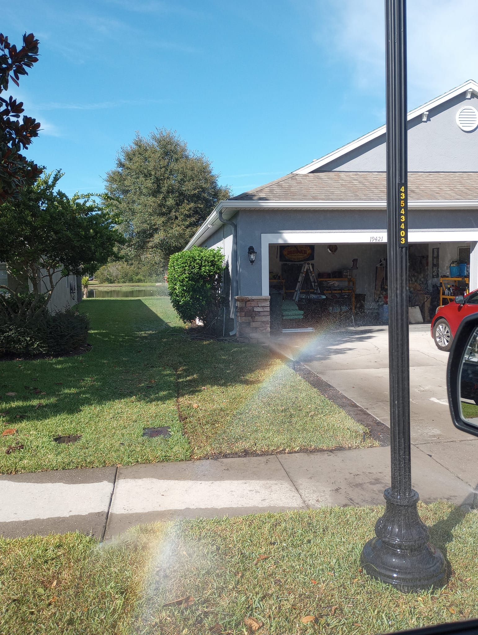 A rainbow arches over a green lawn in front of a blue-gray house. Blue sky.