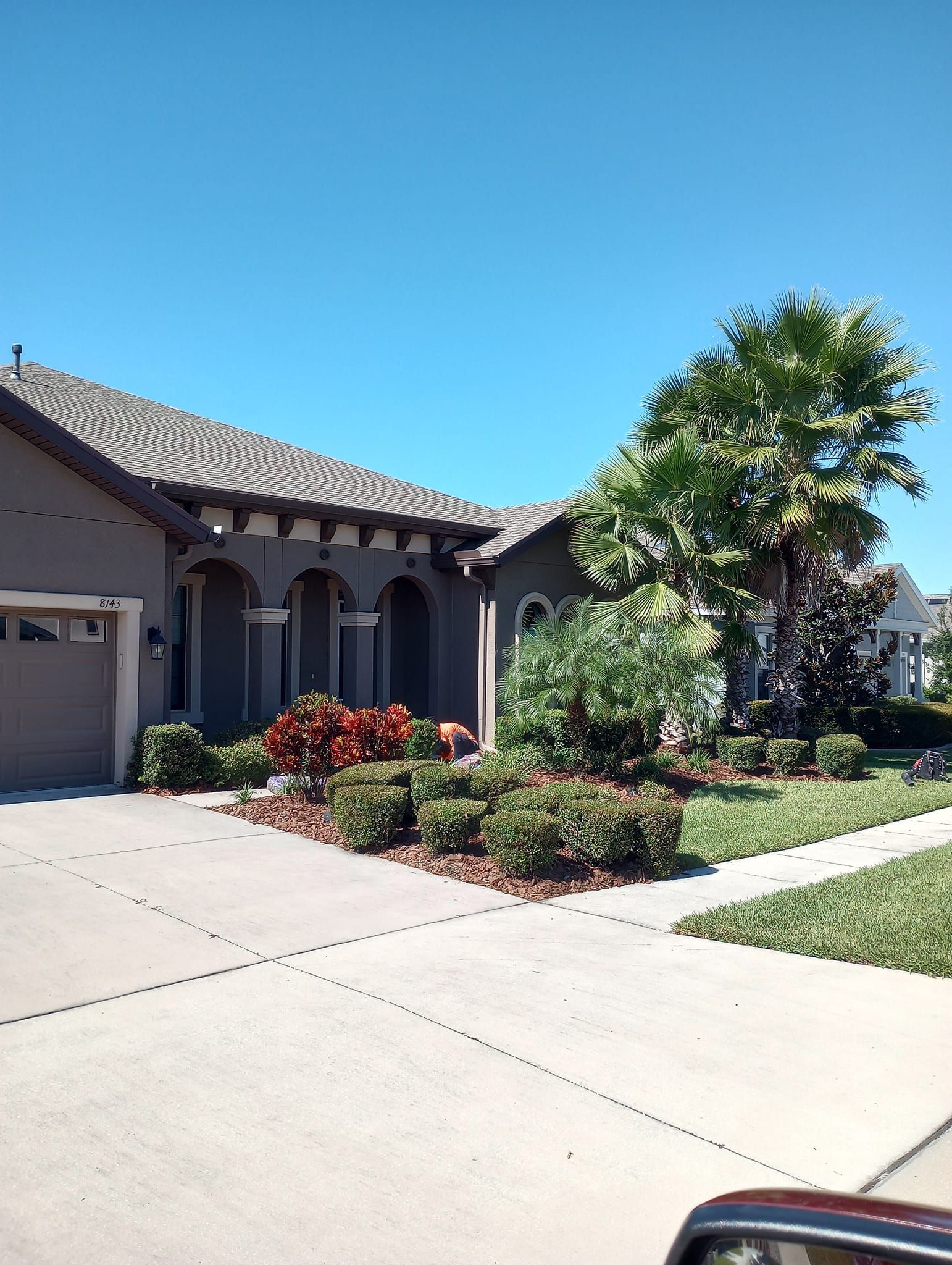 House with gray stucco, driveway, landscaping, and clear blue sky.