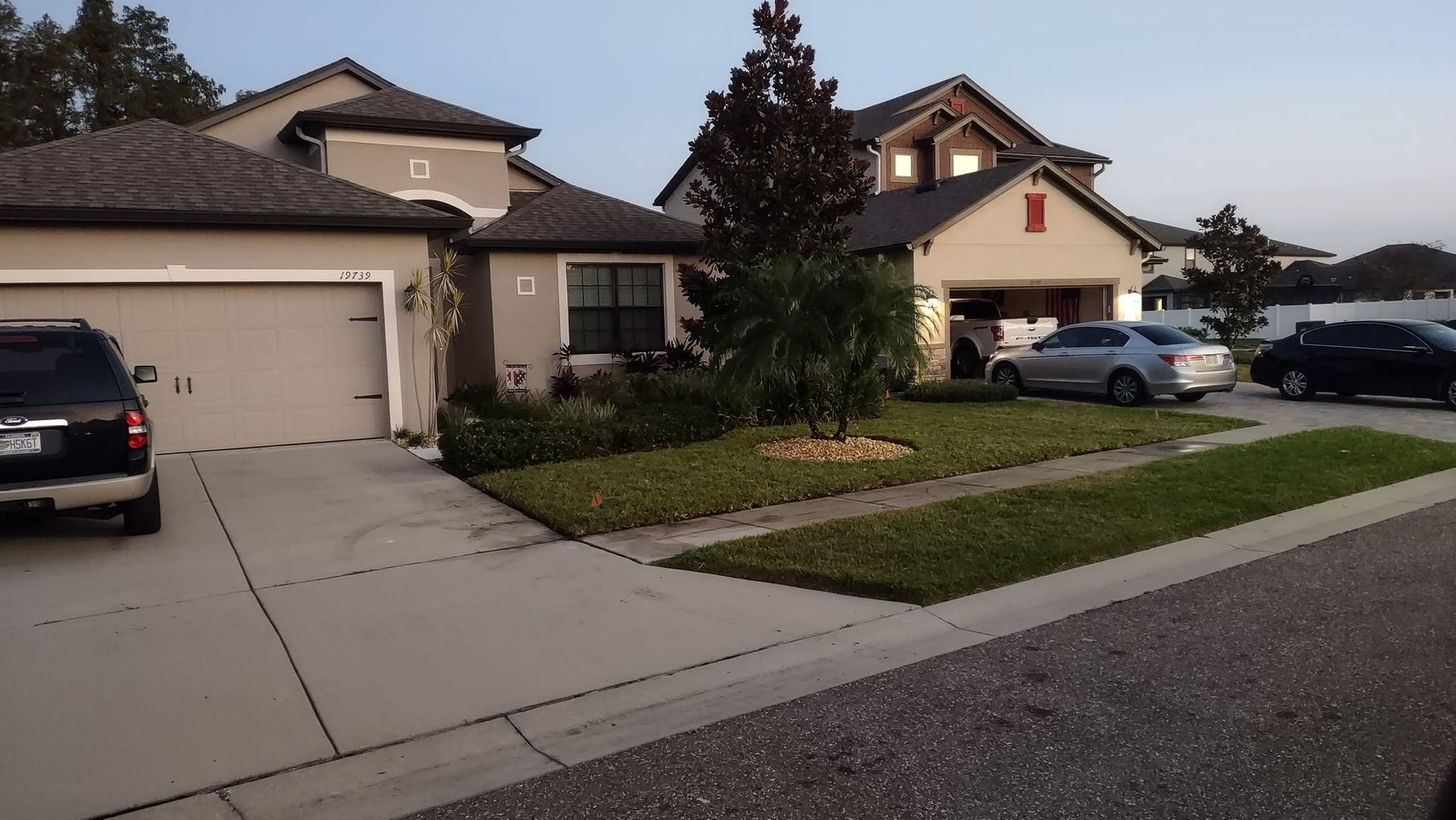 Suburban homes with parked cars in driveways; green lawns and cloudy sky.