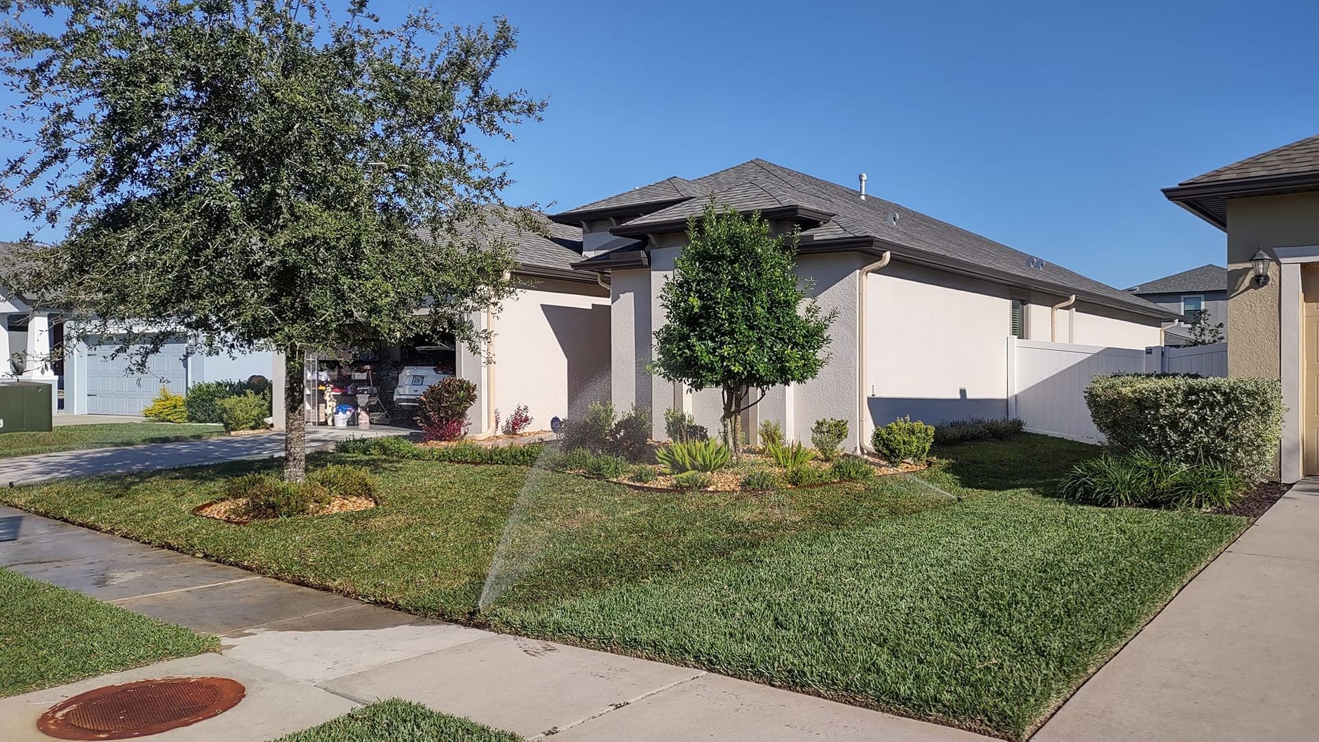 Suburban house with green lawn being watered by sprinklers on a sunny day.
