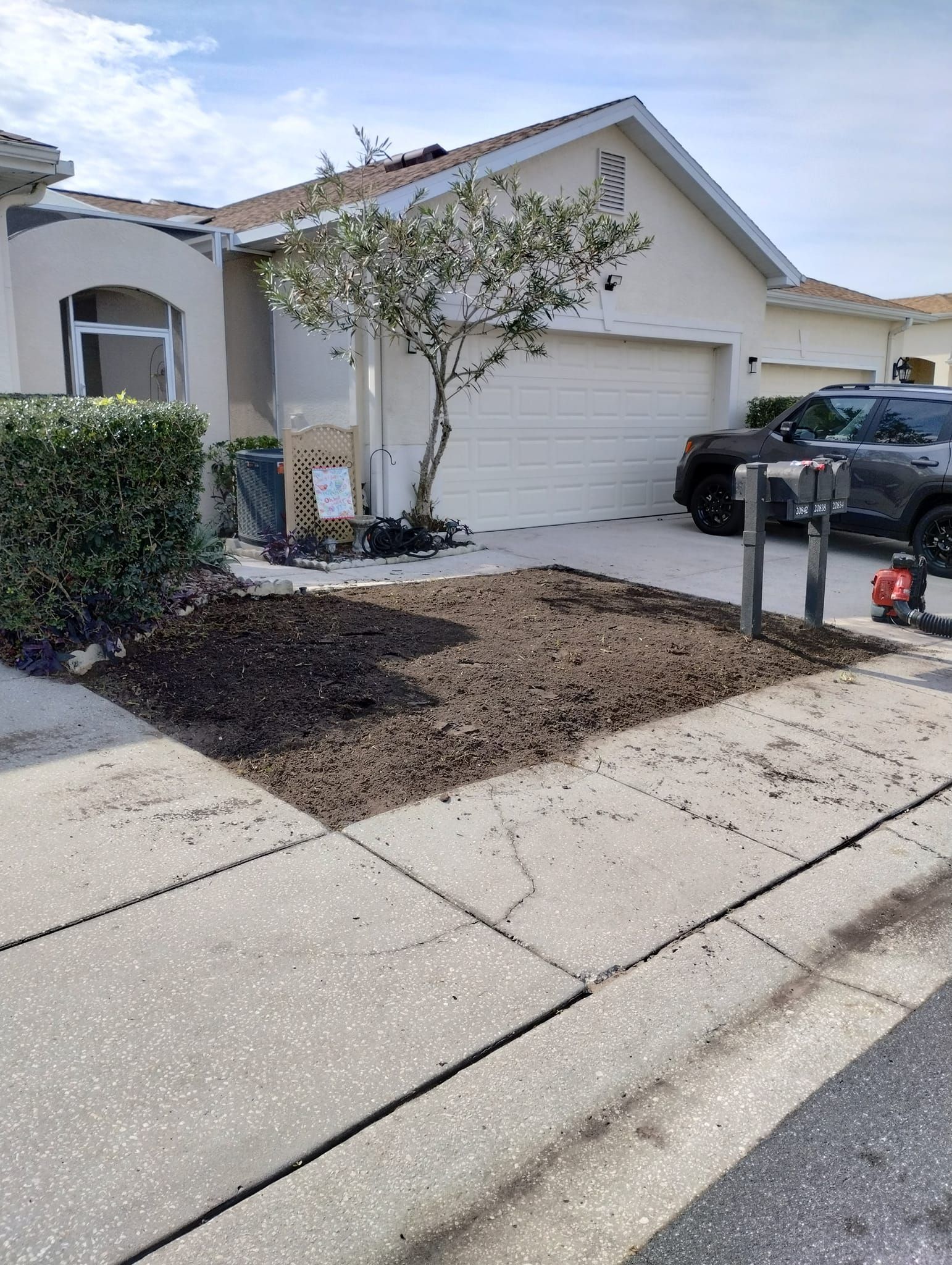Front yard with freshly tilled soil ready for planting, beside a house and driveway.