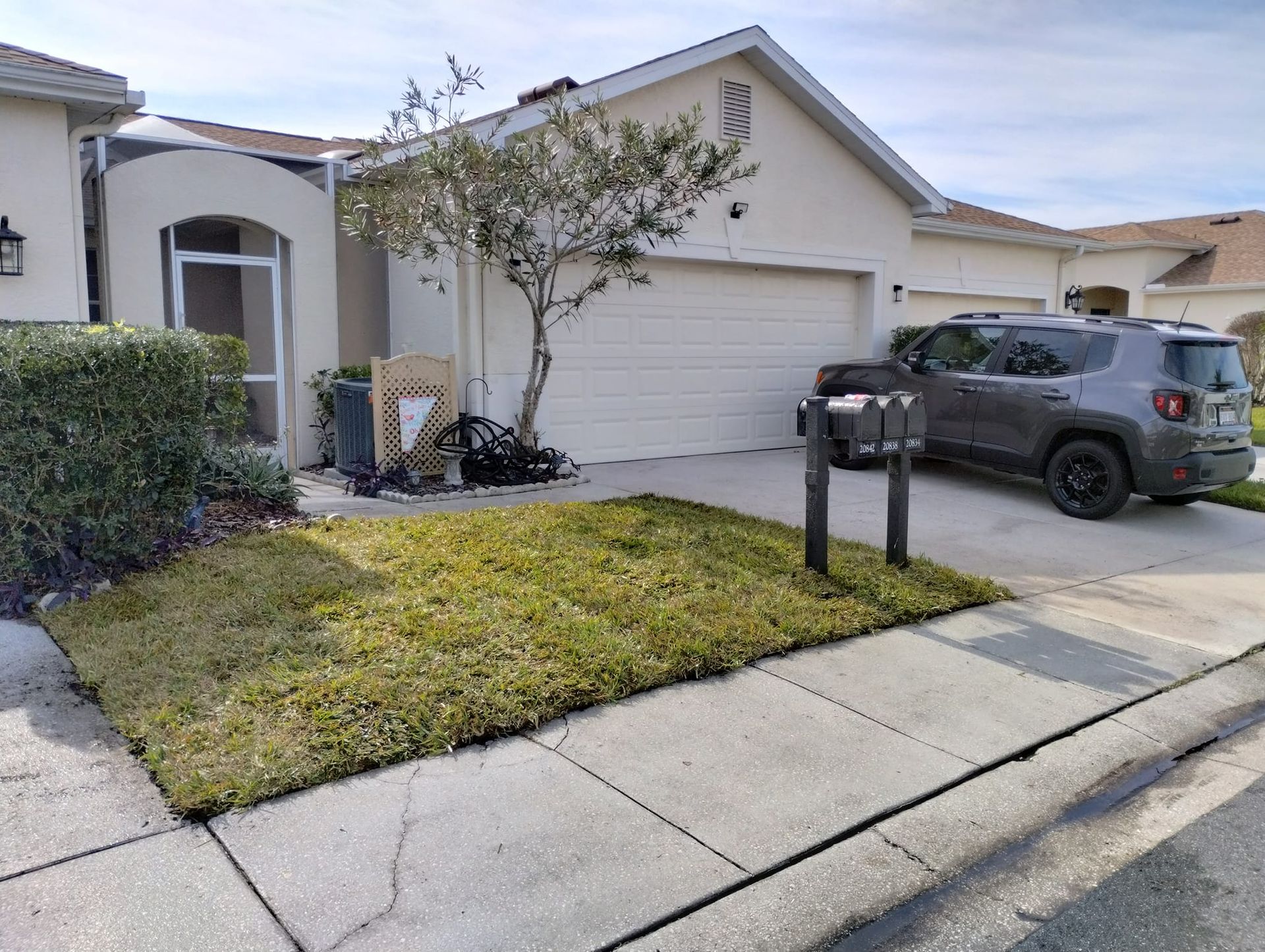Suburban home exterior with garage, lawn, mailbox, and parked SUV. Sidewalk in foreground, partly cloudy sky.