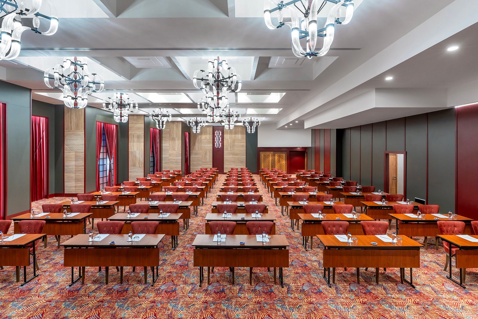 Conference room with rows of orange tables and chairs, chandeliers, and patterned carpet