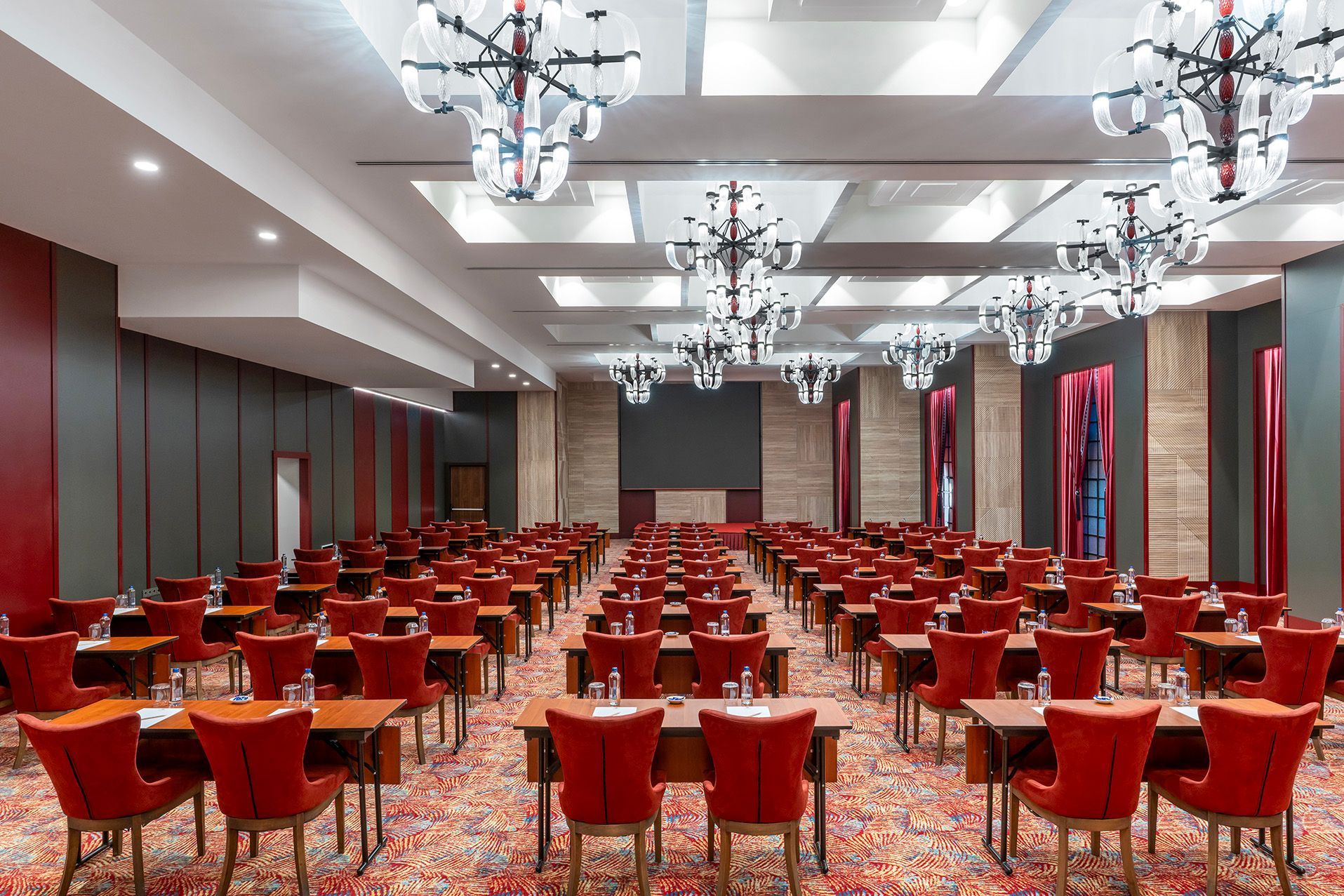 Empty conference hall with rows of red chairs and chandeliers on a patterned carpet