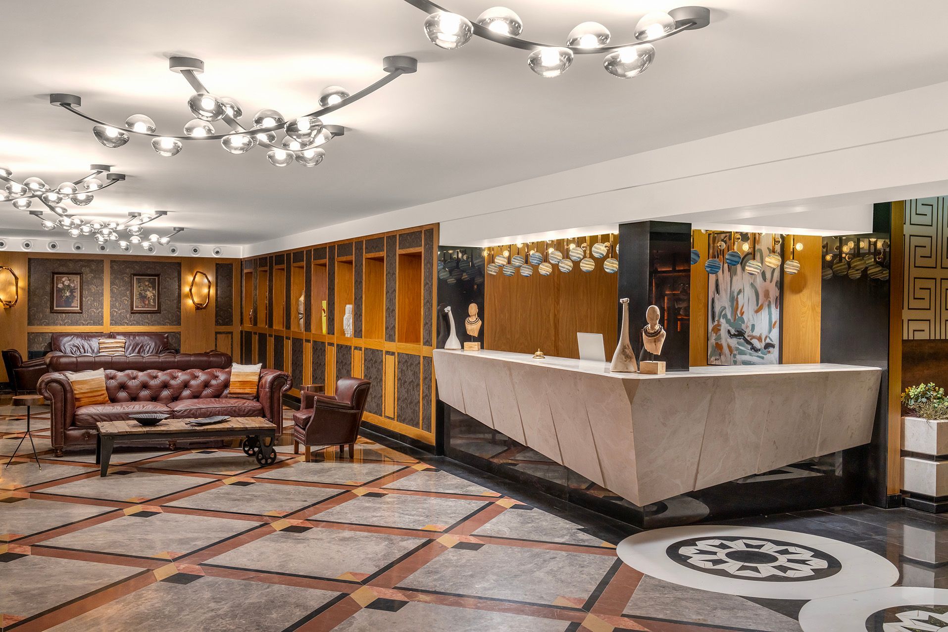 Elegant hotel lobby with patterned carpet, ornate ceiling lights, seating area, and reception desk