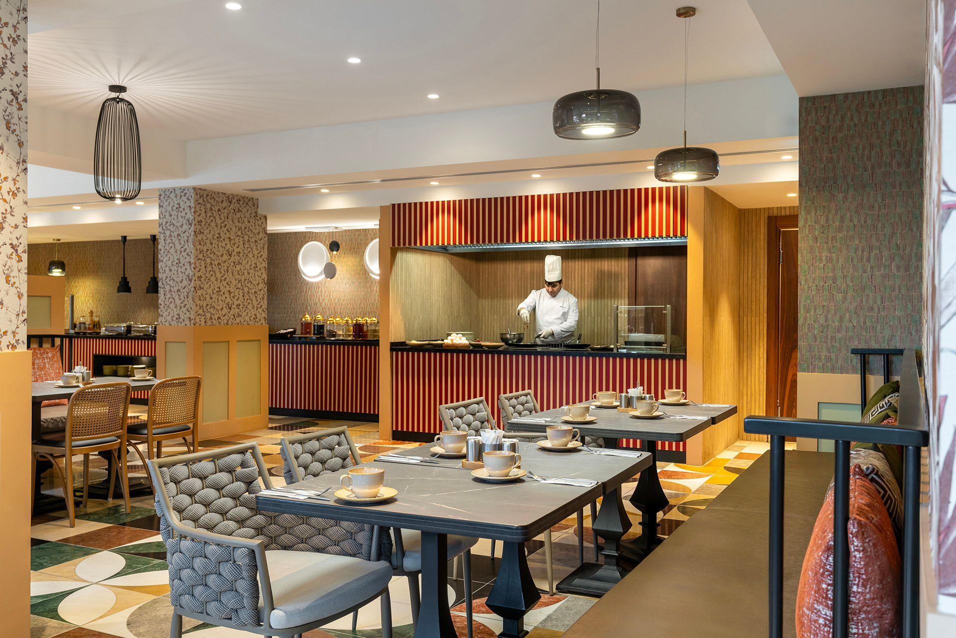 Restaurant dining room with blue chairs, set tables, and a chef behind a red-striped service counter