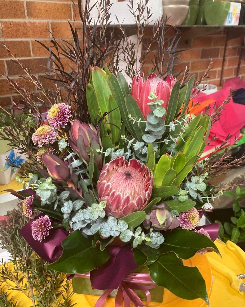 A Vase Filled With Flowers and Leaves is Sitting on a Table — Wingham Nursery and Florist PTY Ltd In Diamond Beach, NSW