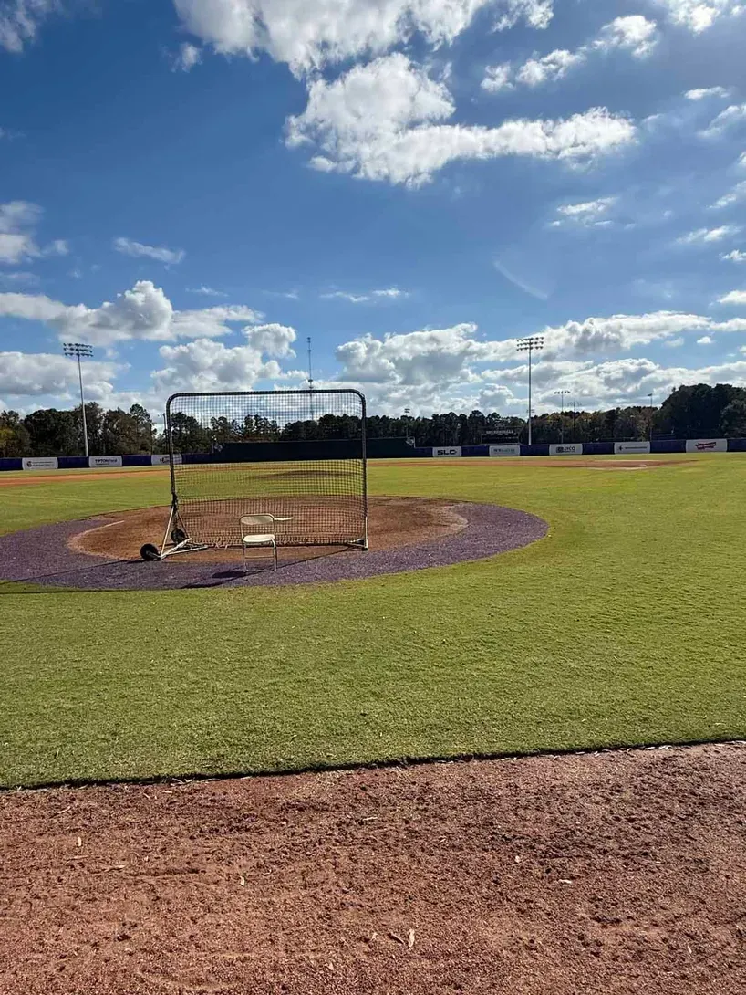 Baseball field with a batting cage and clear sky.