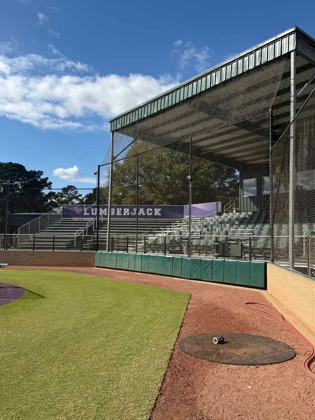 Baseball field with empty bleachers behind a green padded wall; 