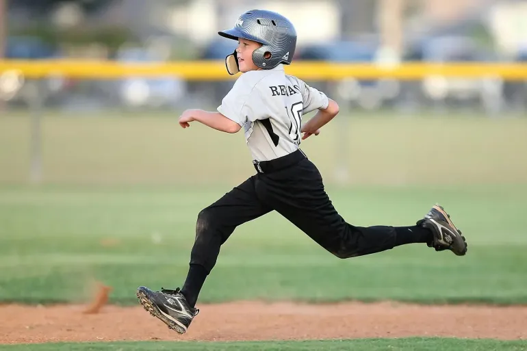 Young baseball player running, wearing helmet and uniform, on a baseball field.