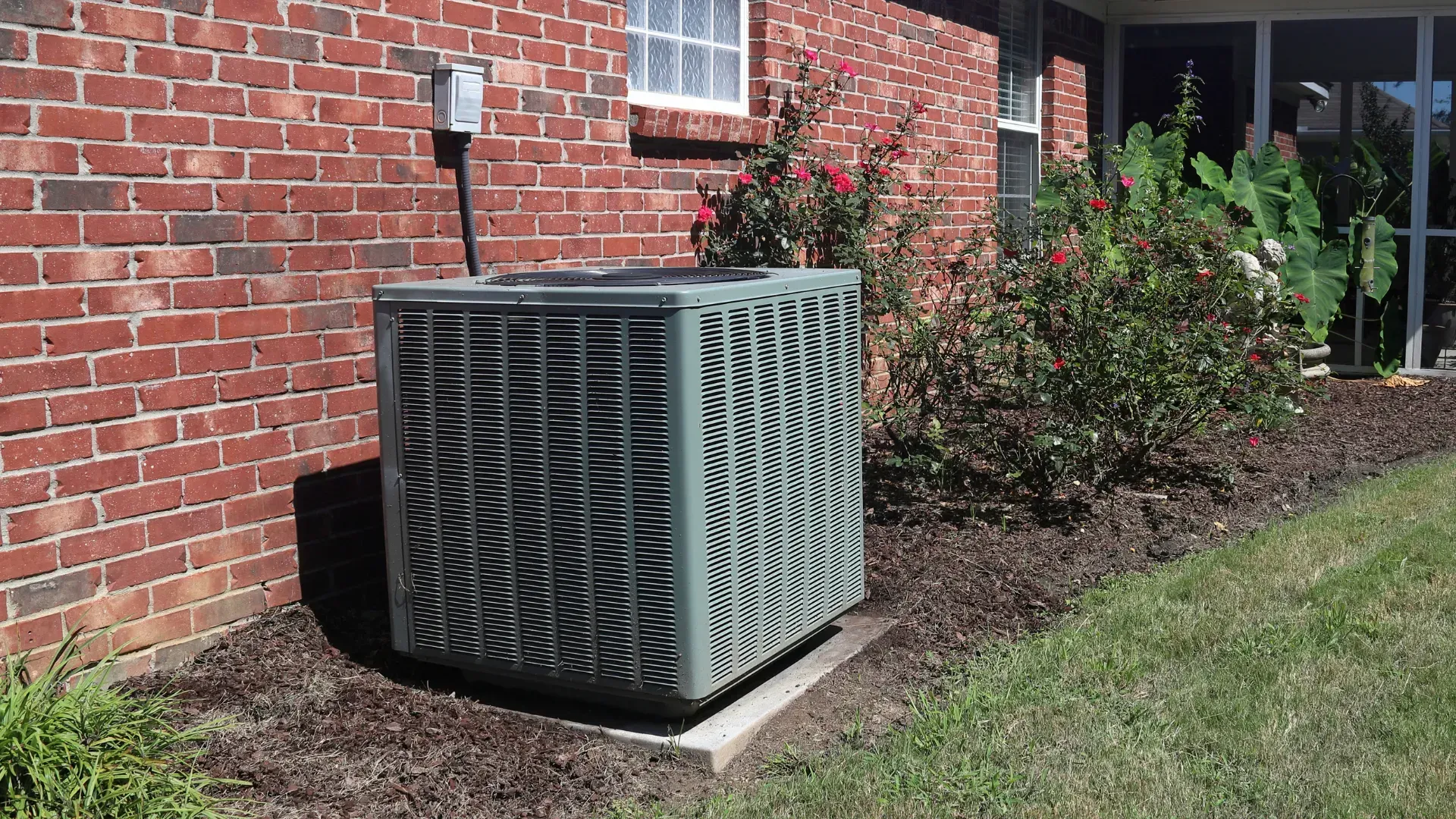 An air conditioner is sitting on the side of a brick house.