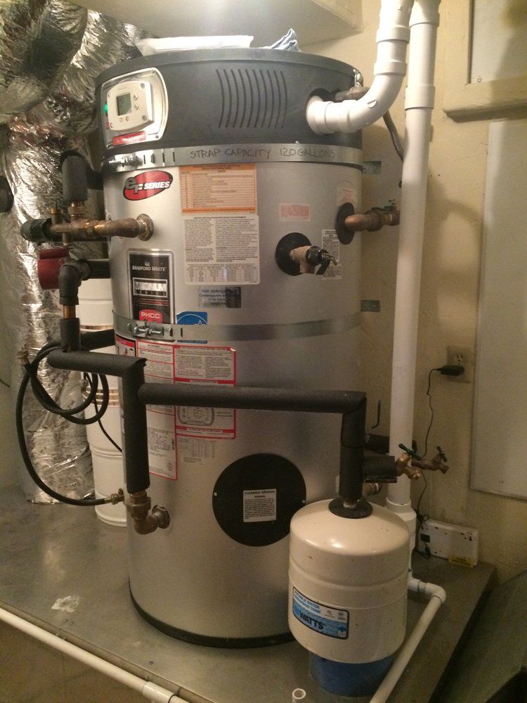 A water heater is sitting on top of a metal table in a basement.