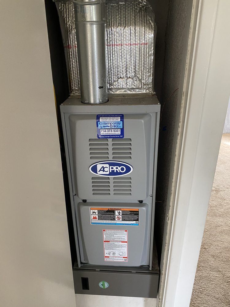 A gray air conditioner is sitting in a corner of a room.