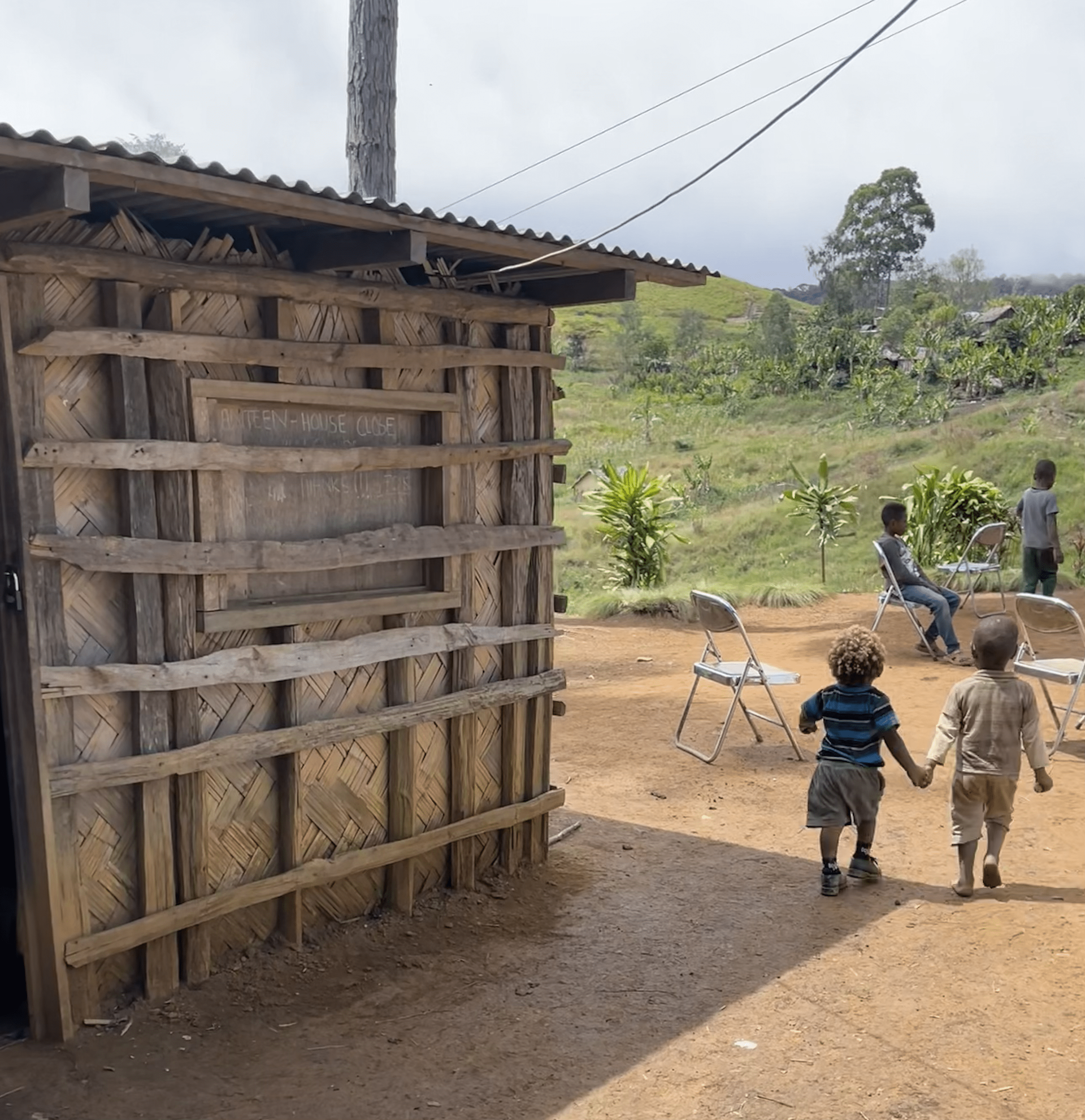 Een groep kinderen staat voor een houten gebouw Papoea-Nieuw-Guinea 