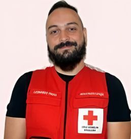 Um homem com barba está vestindo um colete vermelho com uma cruz branca