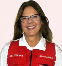 Uma mulher de óculos e colete vermelho está sorrindo.