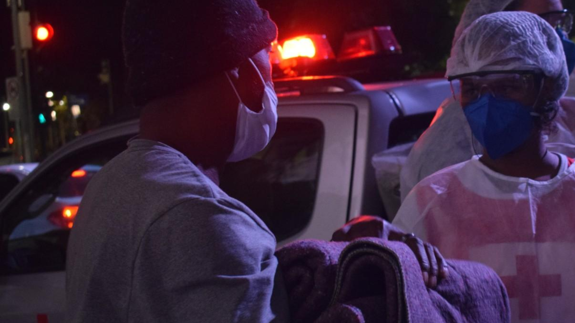 Um homem usando máscara segura um cobertor na frente de uma ambulância.