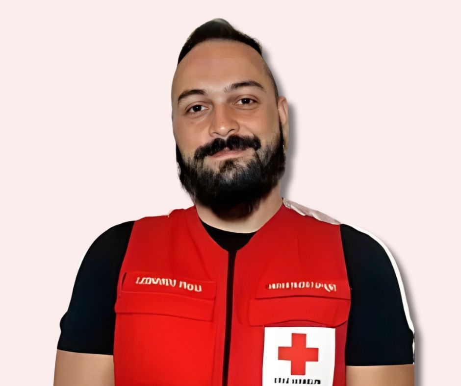 Um homem com barba está vestindo um colete vermelho com uma cruz branca