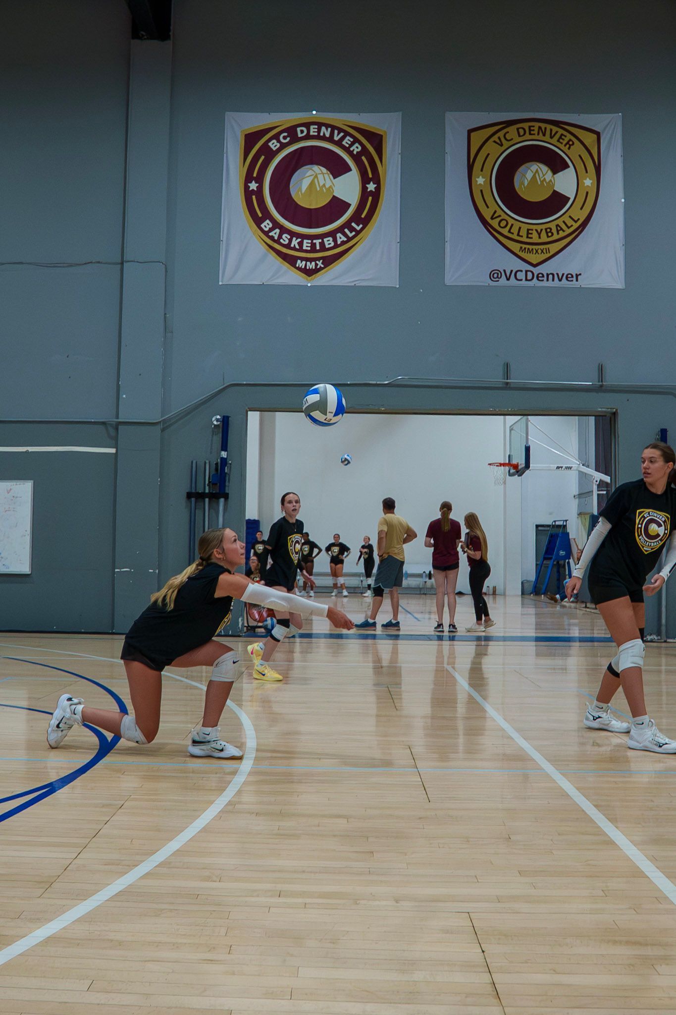 Female volleyball player in black uniform bumping the ball in a blue indoor court.
