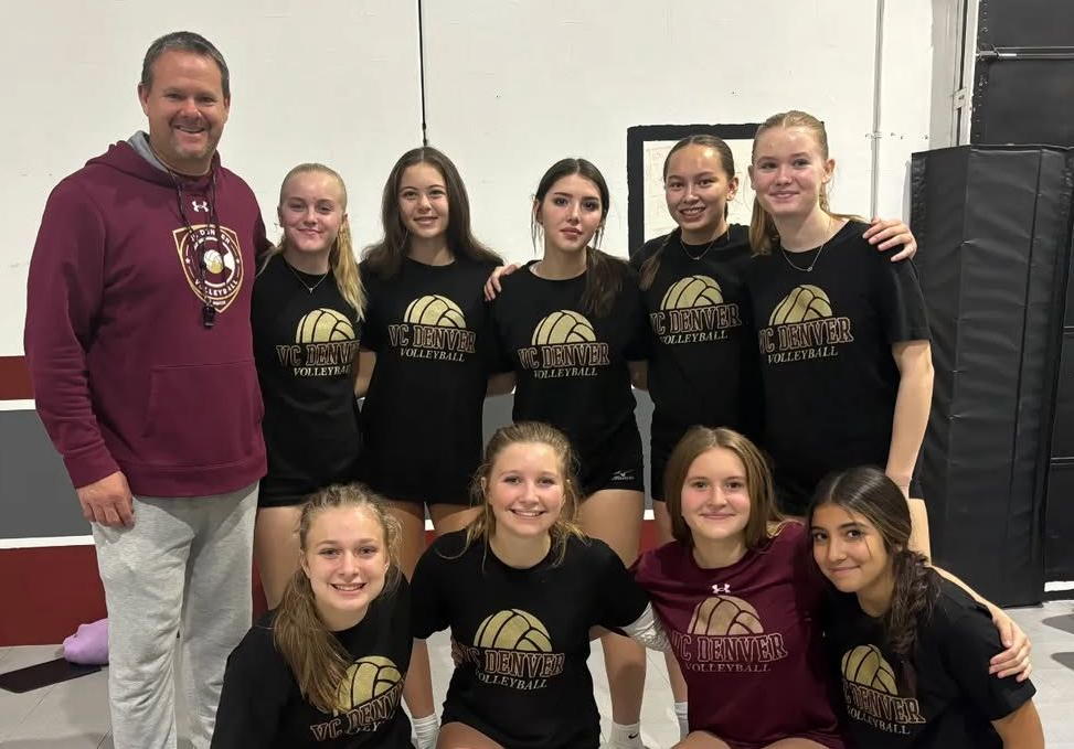 Volleyball team poses with coach. Players in black shirts with gold logo, dark maroon sweats for coach.