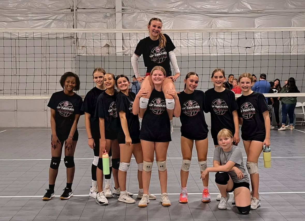 Volleyball player jumping to spike the ball during a game in a gymnasium. Players in black uniforms.
