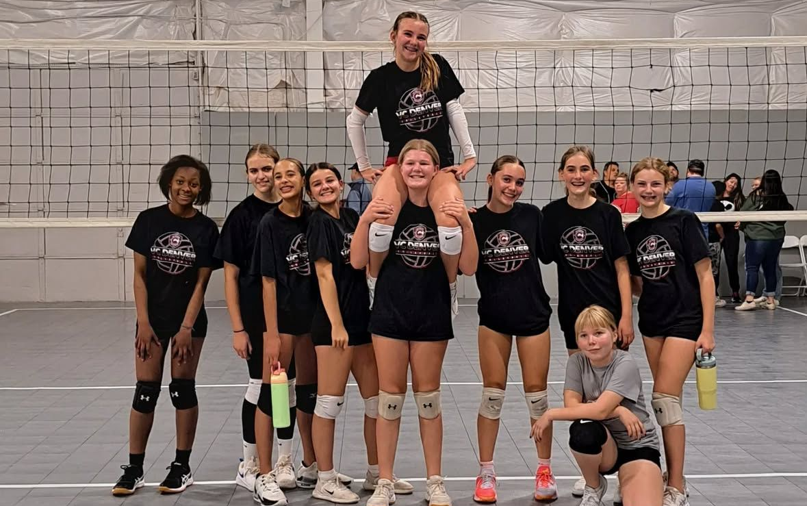 Volleyball team posing for a photo. Some girls are smiling, wearing dark shirts. One girl is on shoulders.