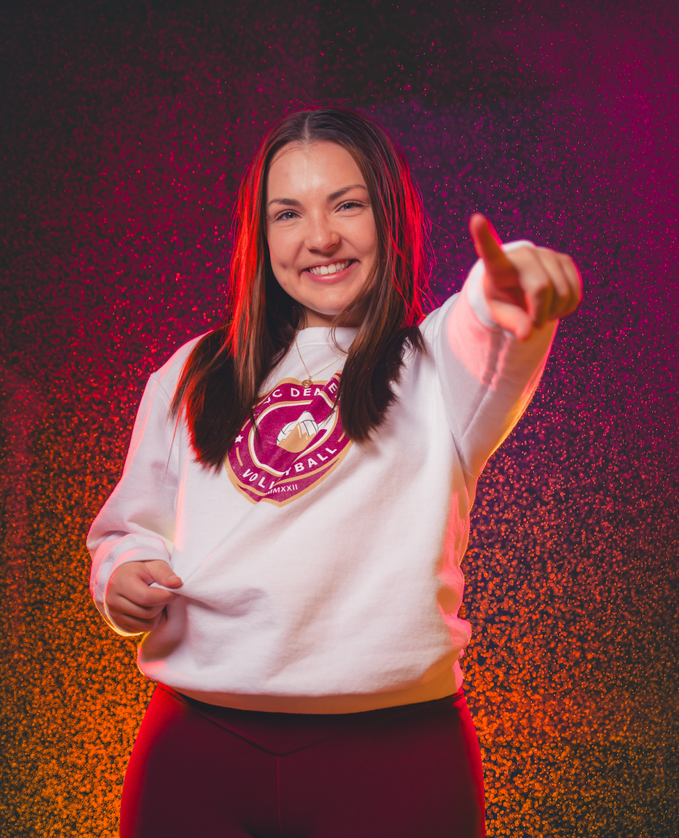 Woman with dark hair and a white shirt smiles outdoors, soft sunlight.