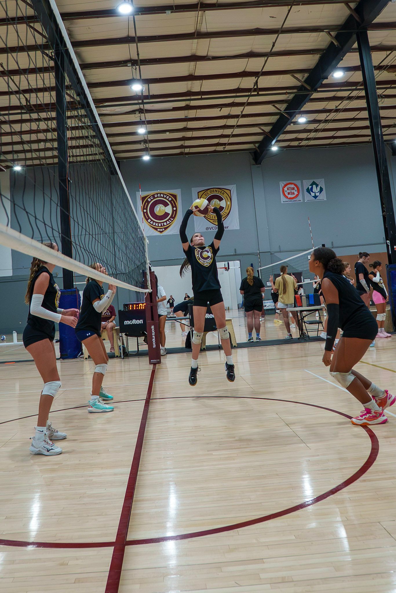 Volleyball player jumping to set the ball during a match, indoor court, black and gold uniform.