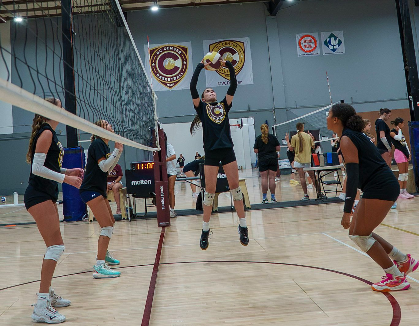 Volleyball player jumping to spike the ball during a game in a gymnasium. Players in black uniforms.