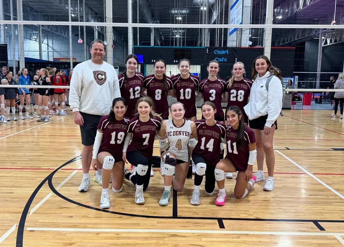 Volleyball team poses on a court. Players and coach wear maroon and white.