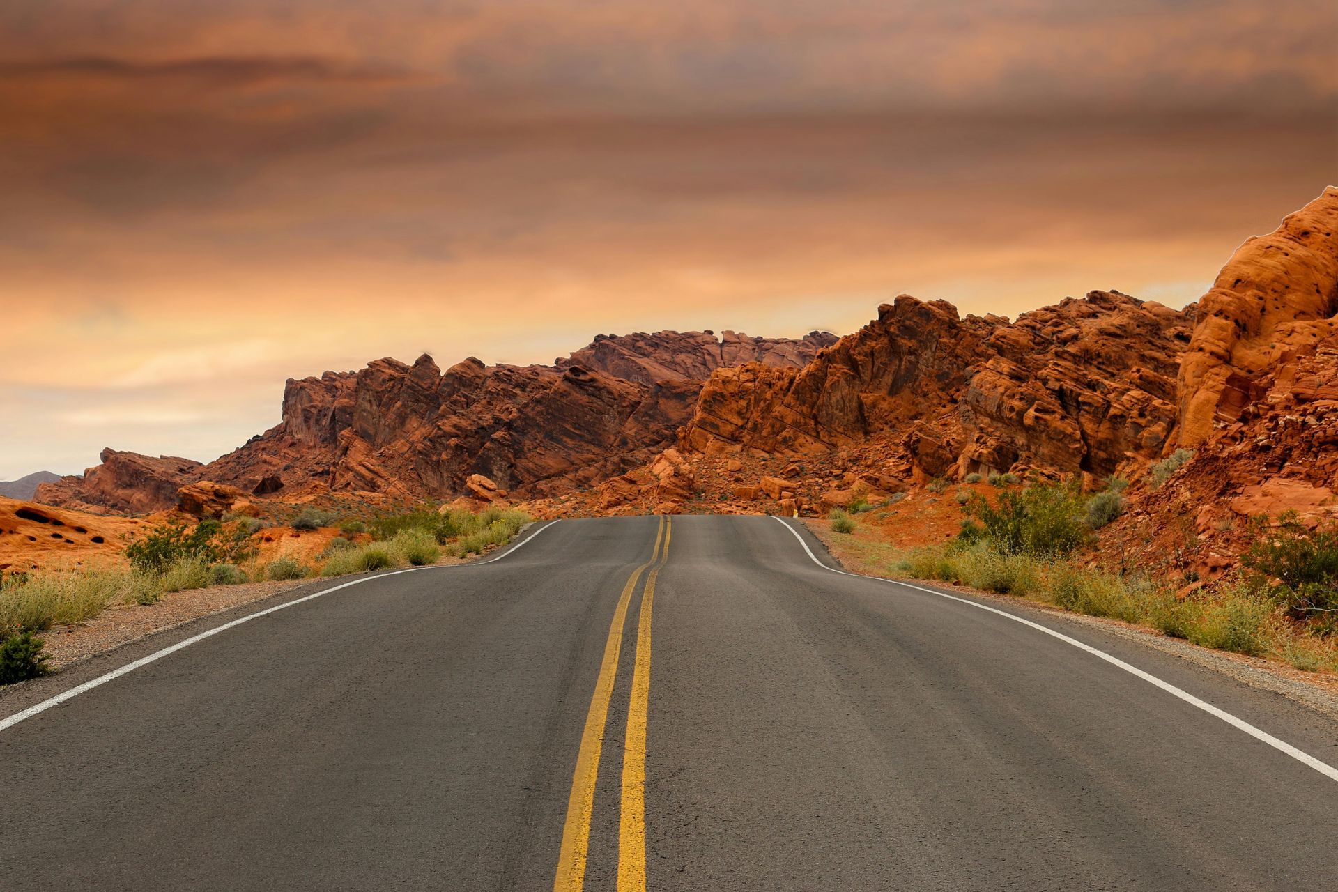 Road through red rock desert landscape under a cloudy sky.
