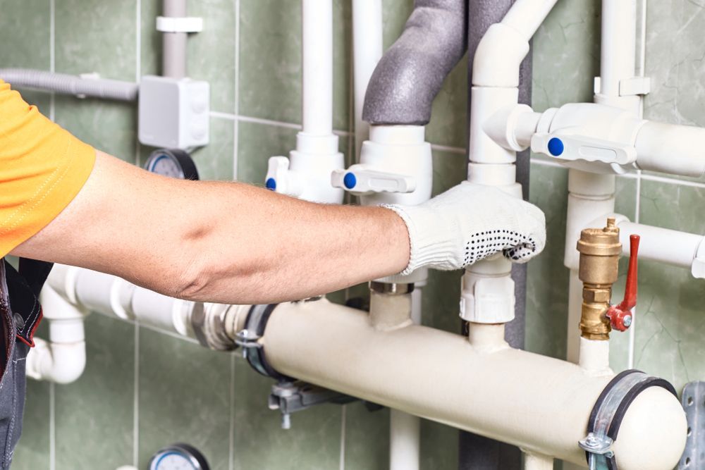 A Person Wearing Work Gloves Adjusting Valves on a White Piping System — Dunnerite Plumbing in Mount Peter, QLD
