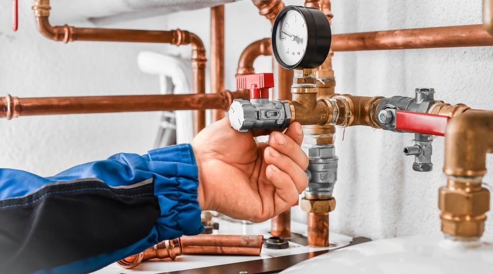 A Person in a Blue Uniform Turns a Silver Valve on a Copper Pipe System — Dunnerite Plumbing in Mount Peter, QLD