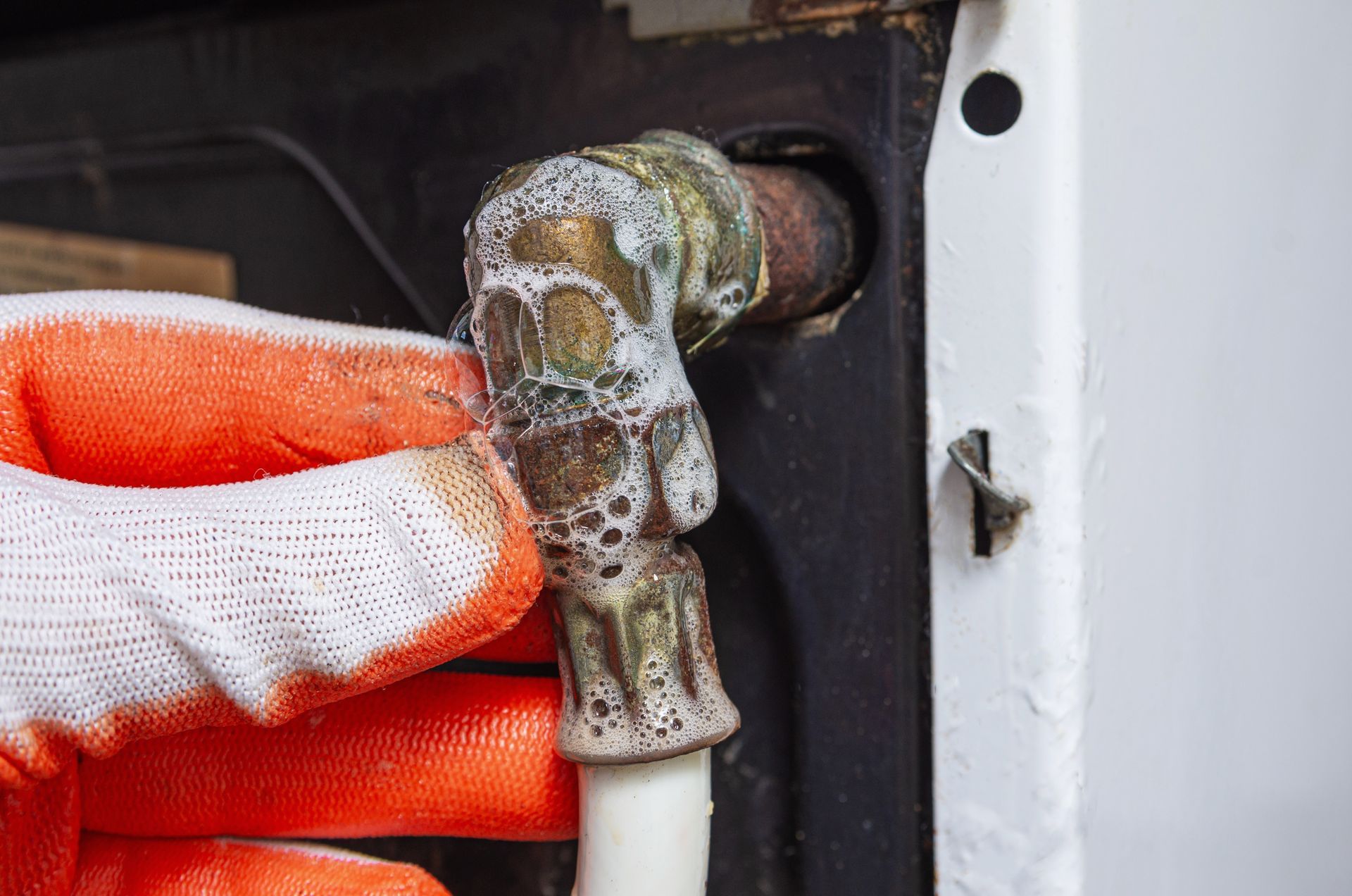 A Person Wearing Orange and White Work Gloves Inspecting a Corroded Brass Plumbing — Dunnerite Plumbing in Edmonton, QLD