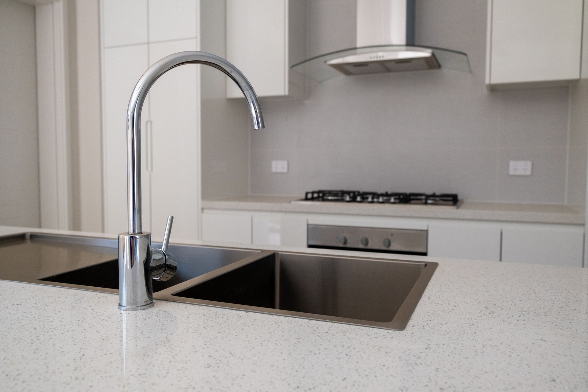 Modern kitchen with stainless steel sink and curved faucet on a light countertop — Dunnerite Plumbing in Edmonton, QLD