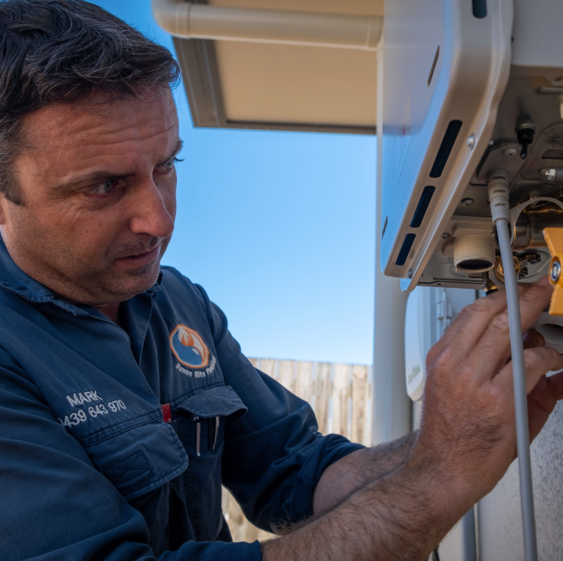A Technician in a Blue Shirt and White Cap Adjusts Red-insulated Plumbing Pipes — Dunnerite Plumbing in Smithfield, QLD
