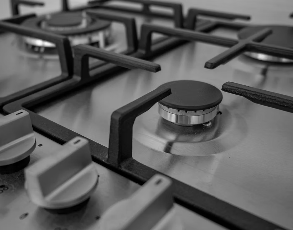 Close-up of a stainless steel gas cooktop with black grates and silver control knobs — Dunnerite Plumbing in Edmonton, QLD