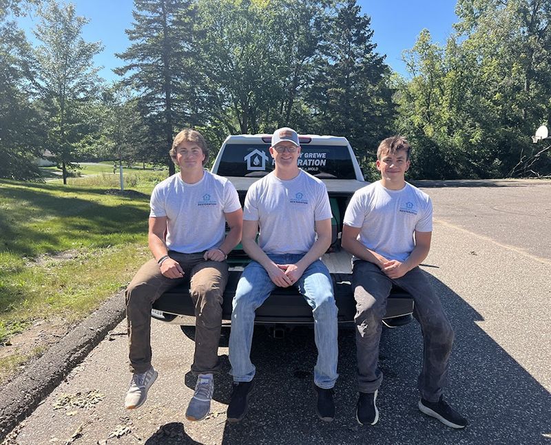 Three young men are sitting on the back of a truck.