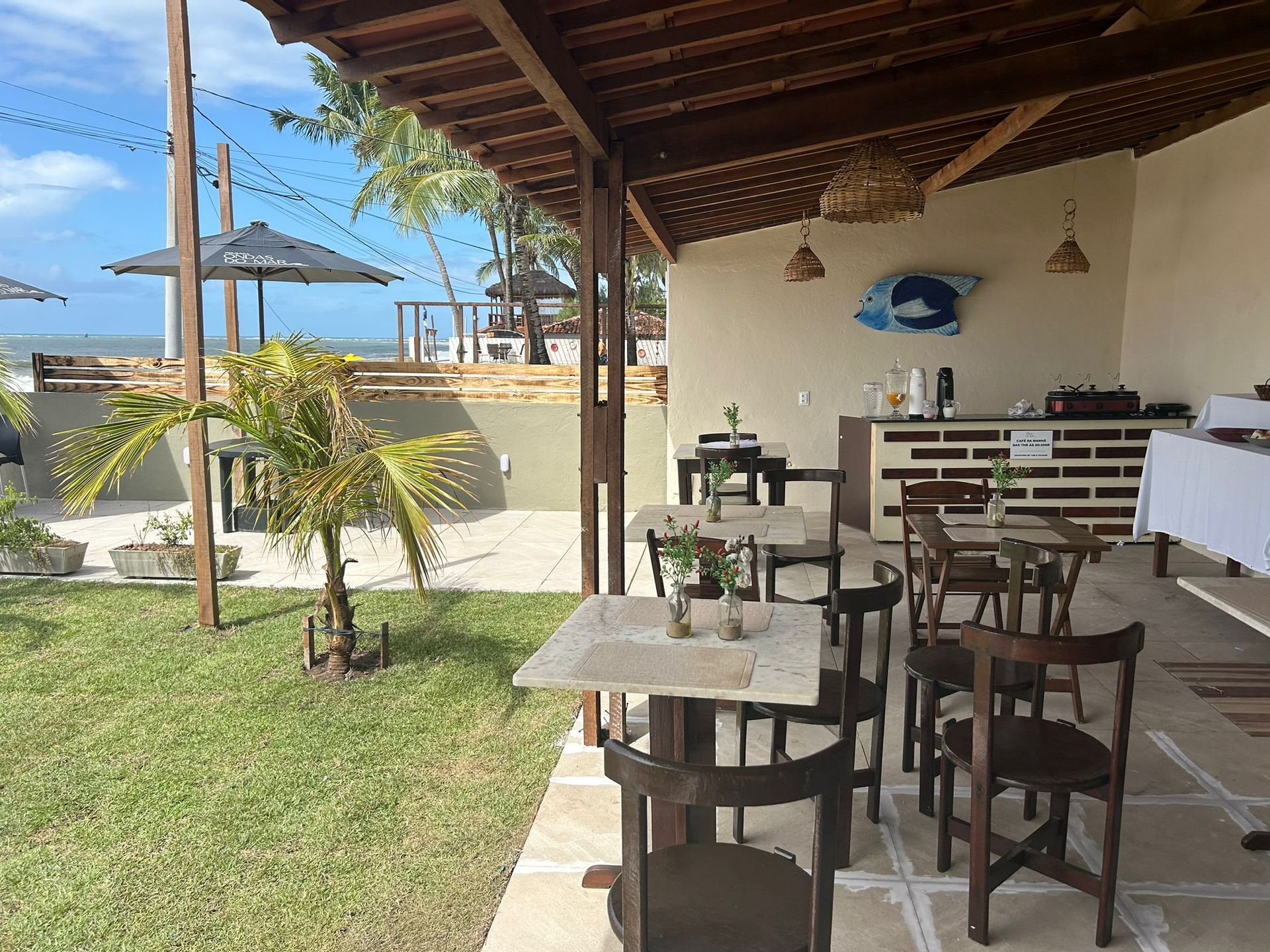 Um restaurante com mesas e cadeiras sob um dossel com vista para o oceano.