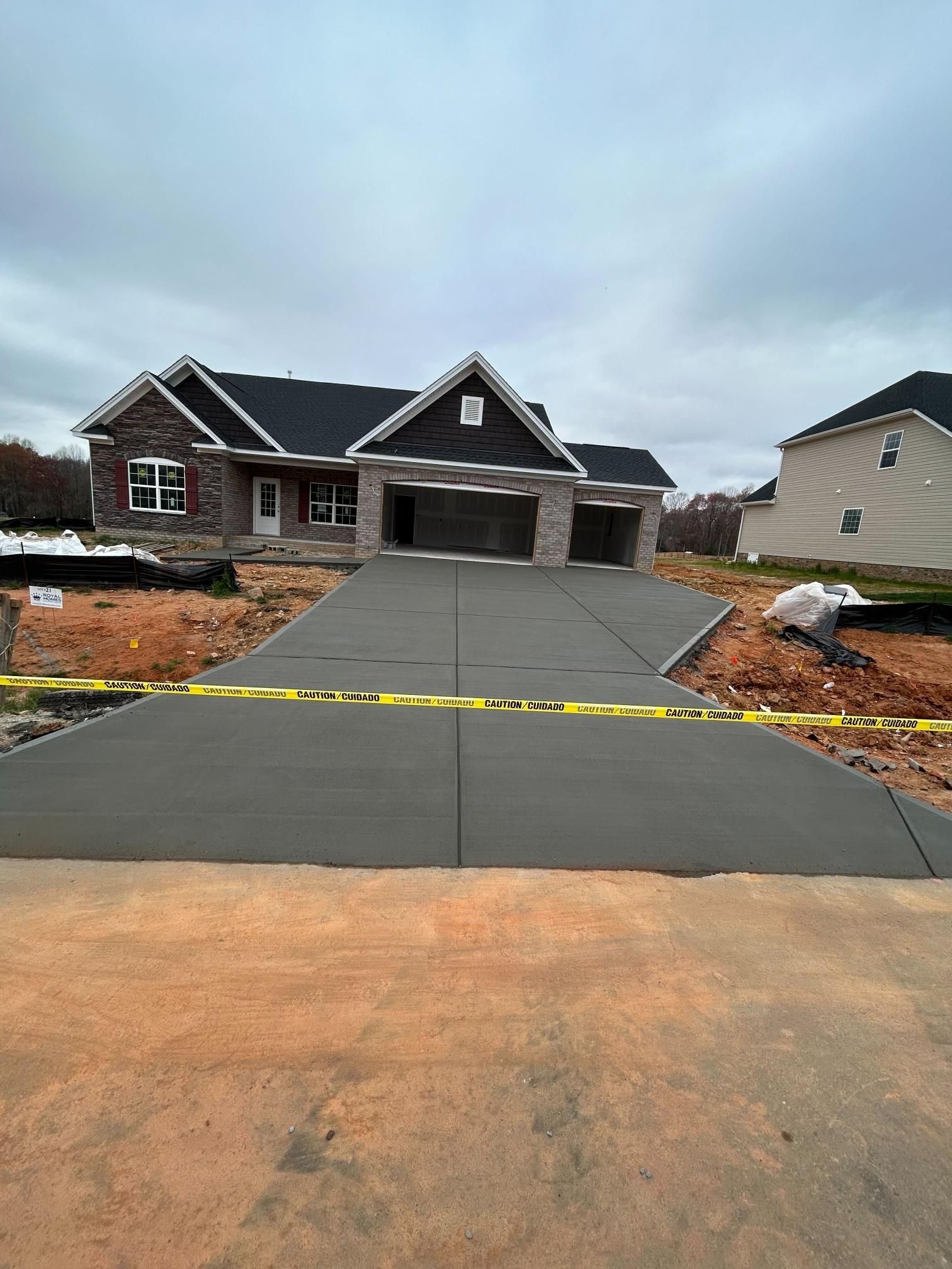 New concrete driveway in front of a brick house under construction; yellow caution tape surrounds the driveway.
