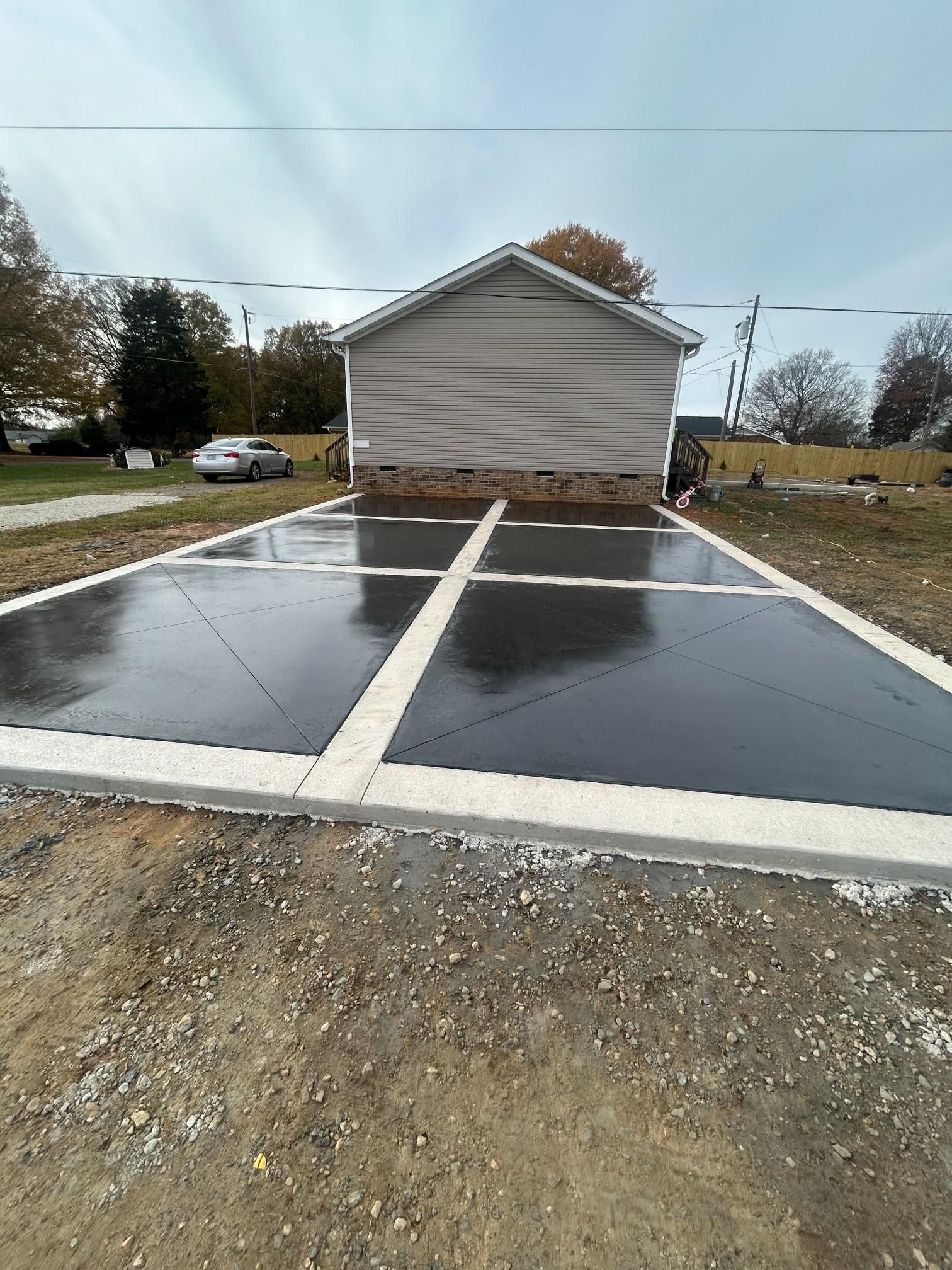 Freshly poured black concrete with white dividers and a house in the background.