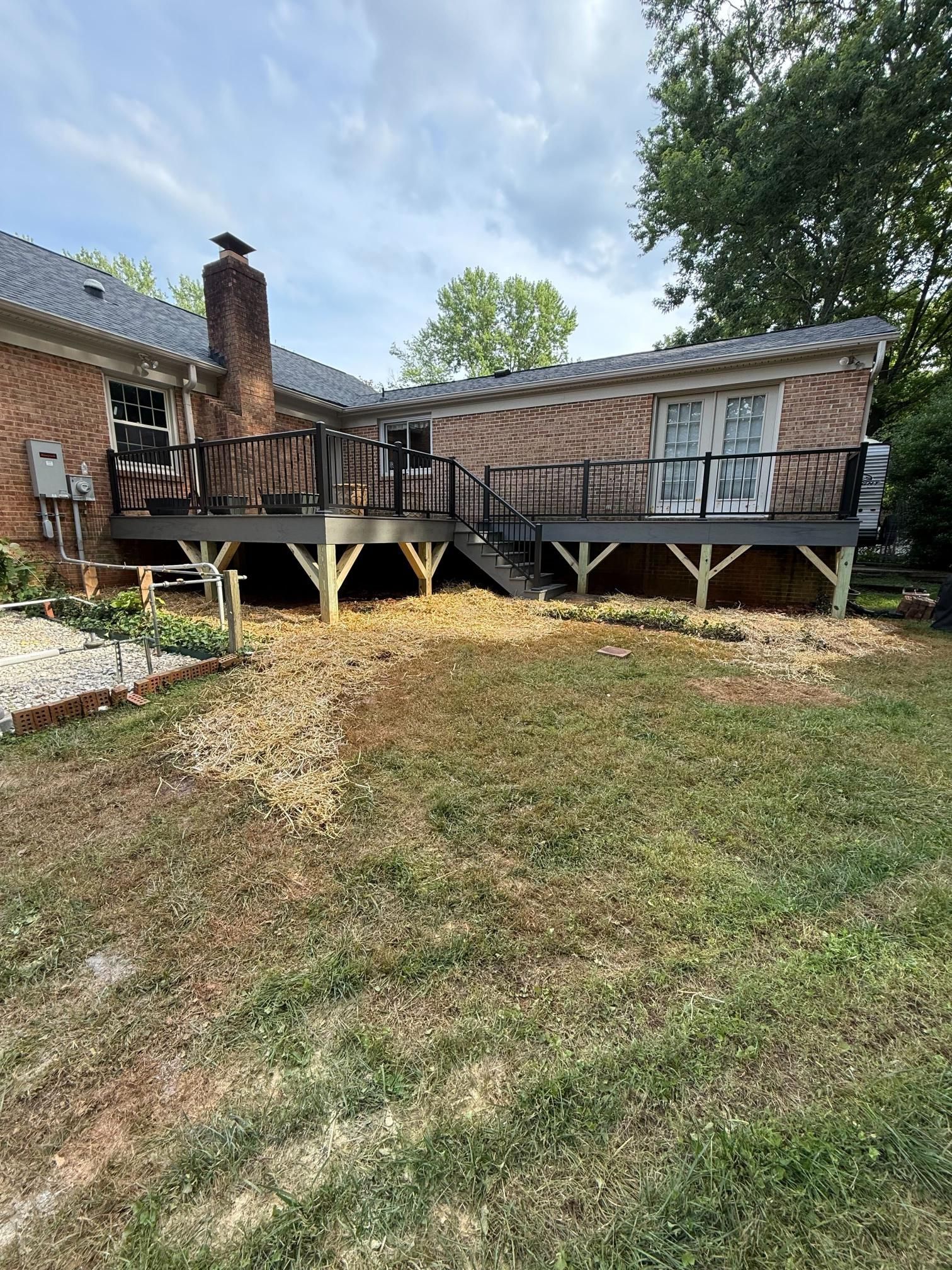 Backyard view with a large wooden deck attached to a brick house, with brown and gray decking and railings.
