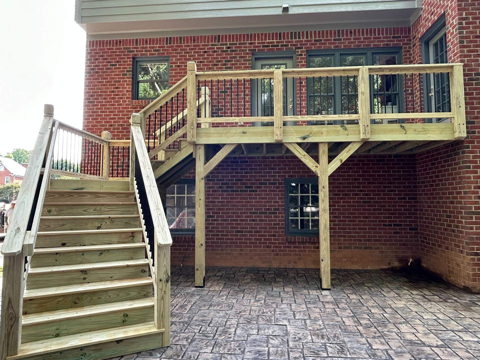 A wooden deck with stairs attached to a red brick building.