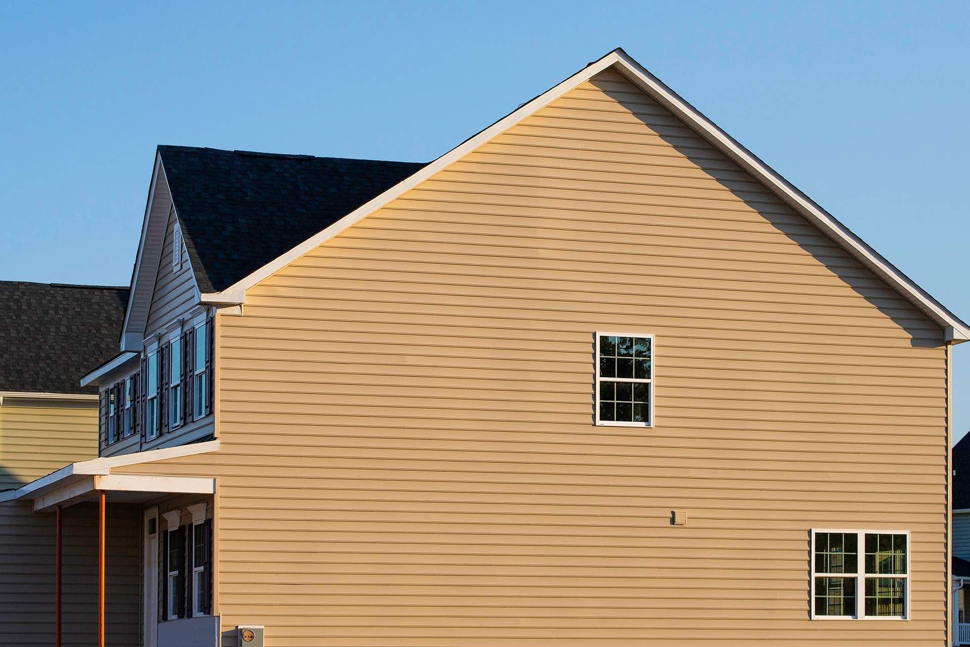 Beige house with a dark roof, windows, and a blue sky.