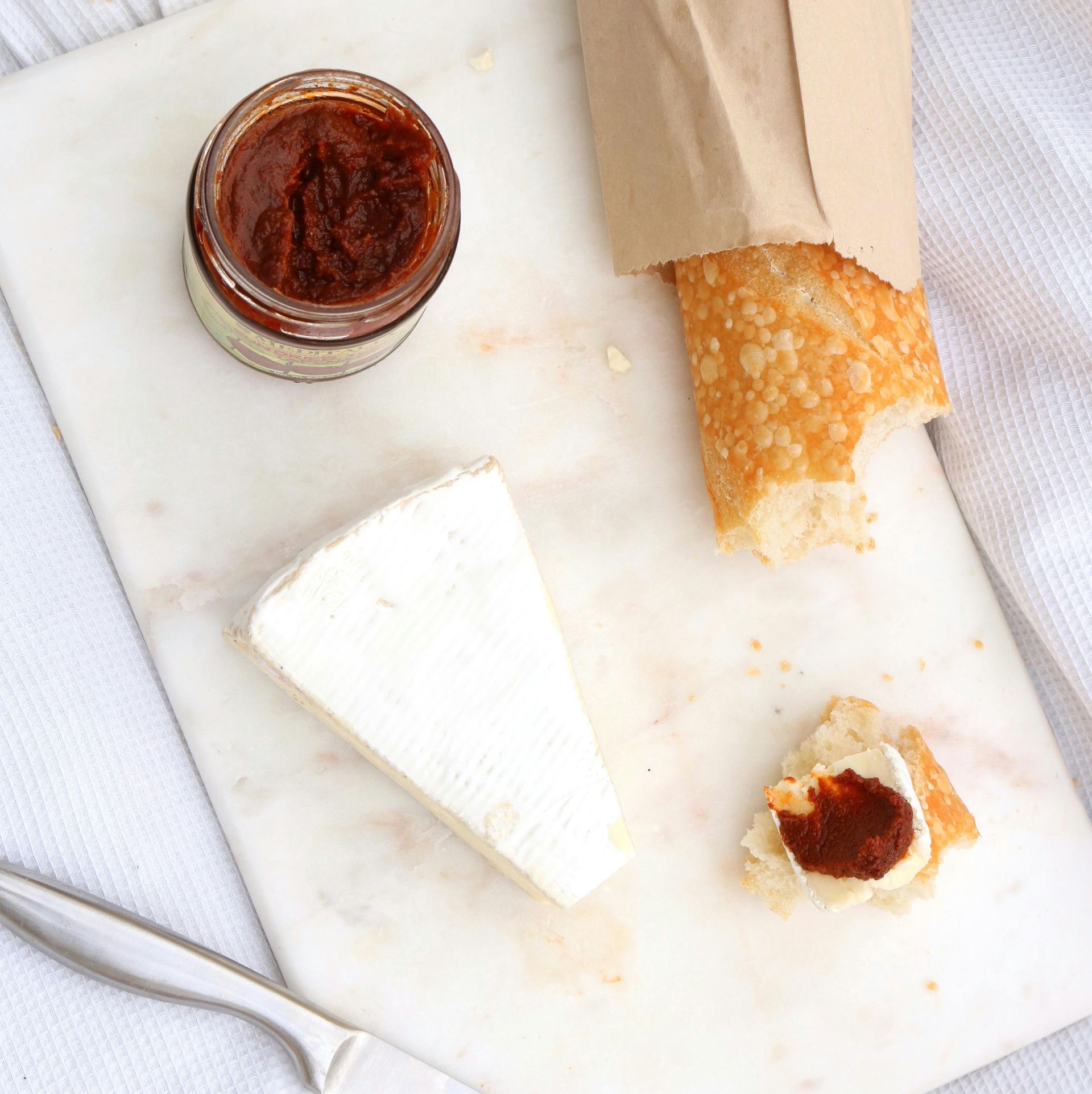 A cheese board with brie, baguette, and a jar of red spread.