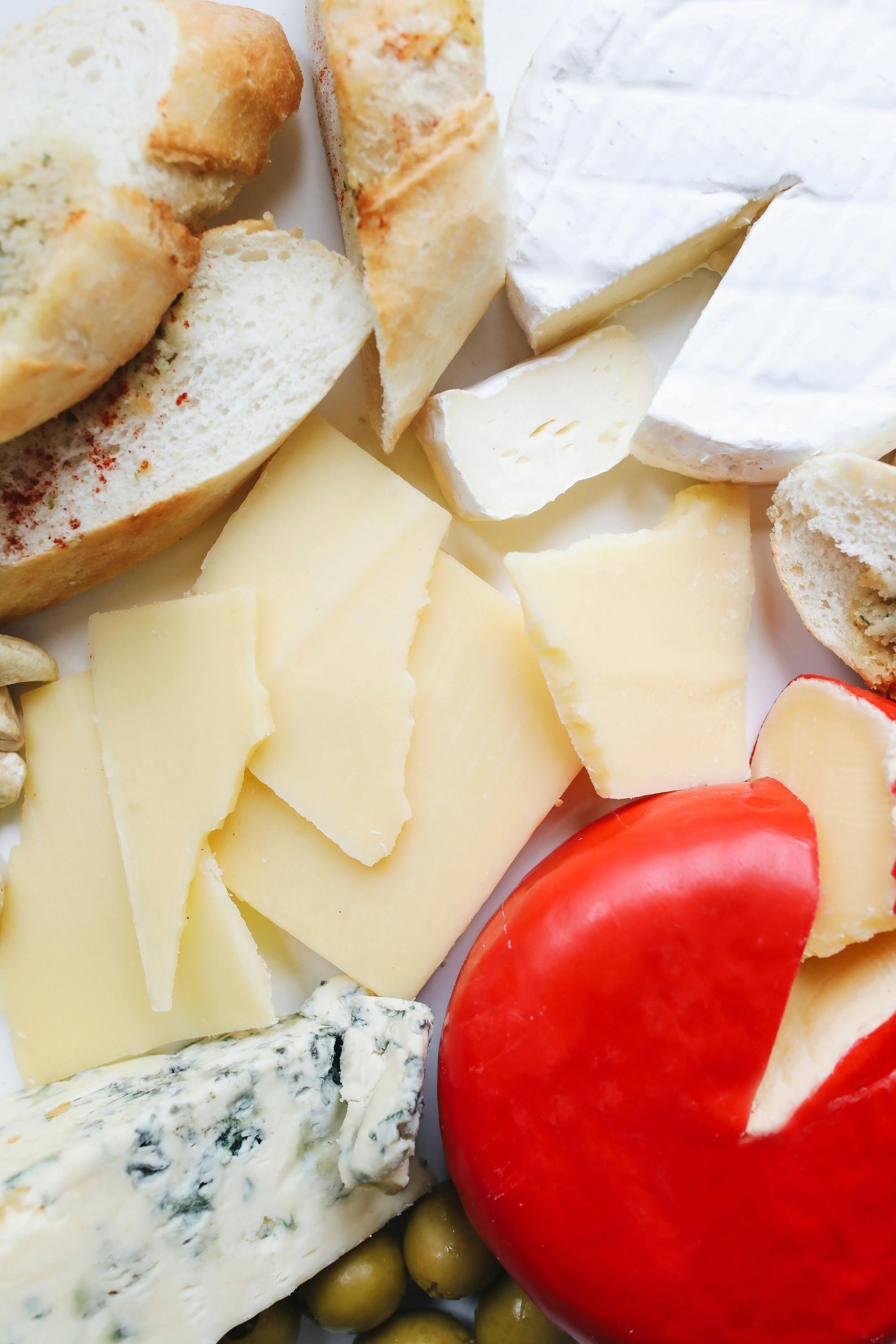Cheese and bread platter with assorted cheeses, bread slices, and olives.