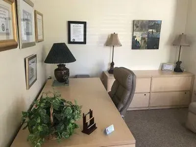 A room with a desk , chair , lamp , and a plant.