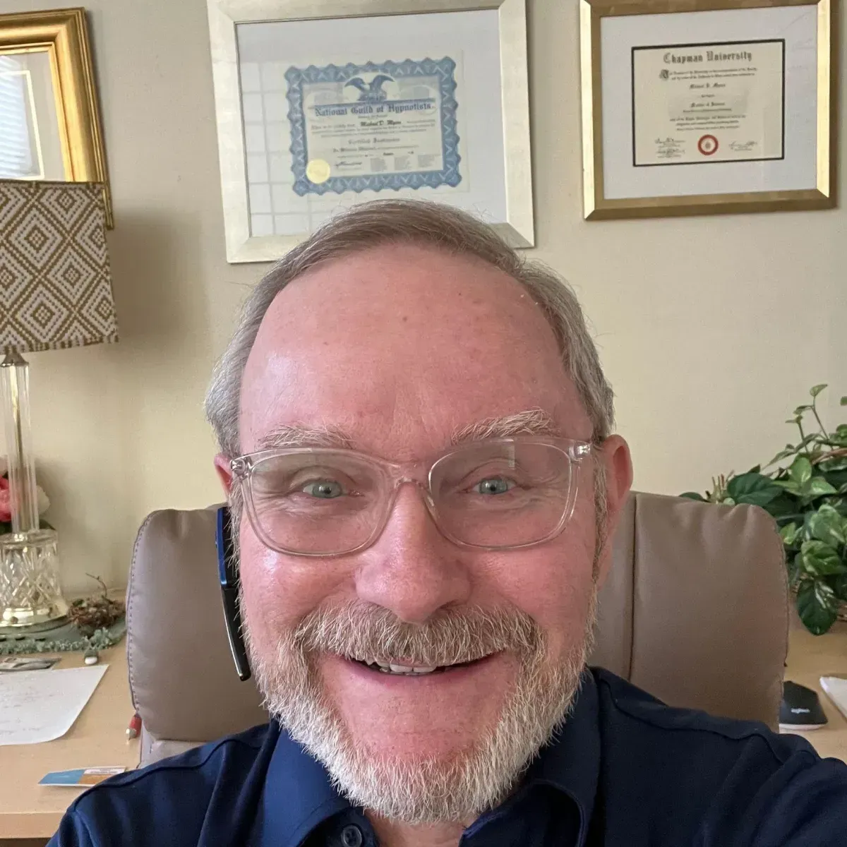 A man with glasses and a beard is smiling while sitting in a chair.