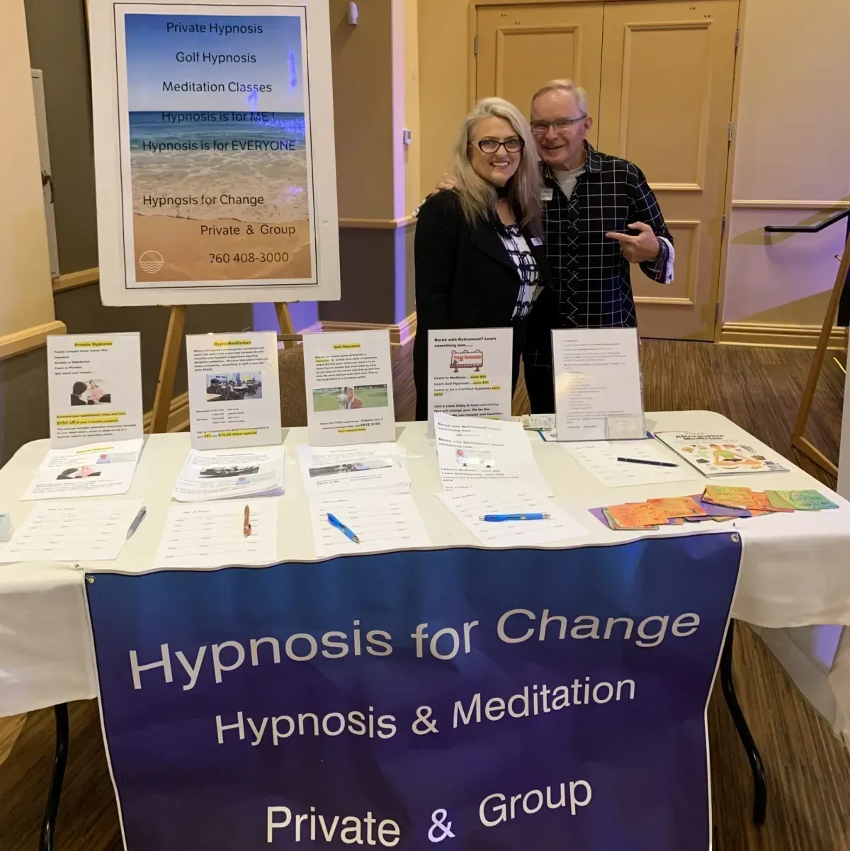 Two people stand behind a table that says hypnosis for change