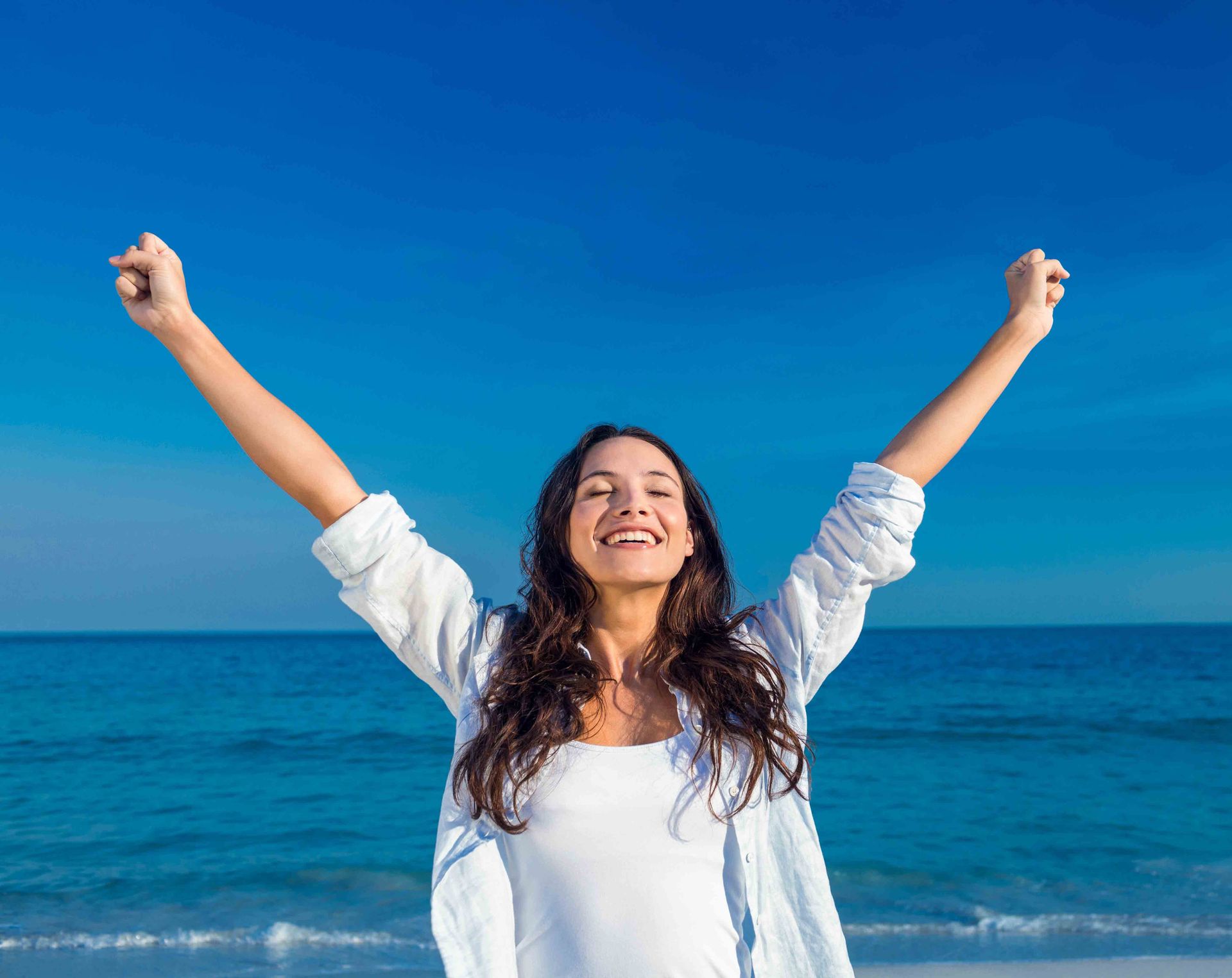 A woman is standing on the beach with her arms in the air.